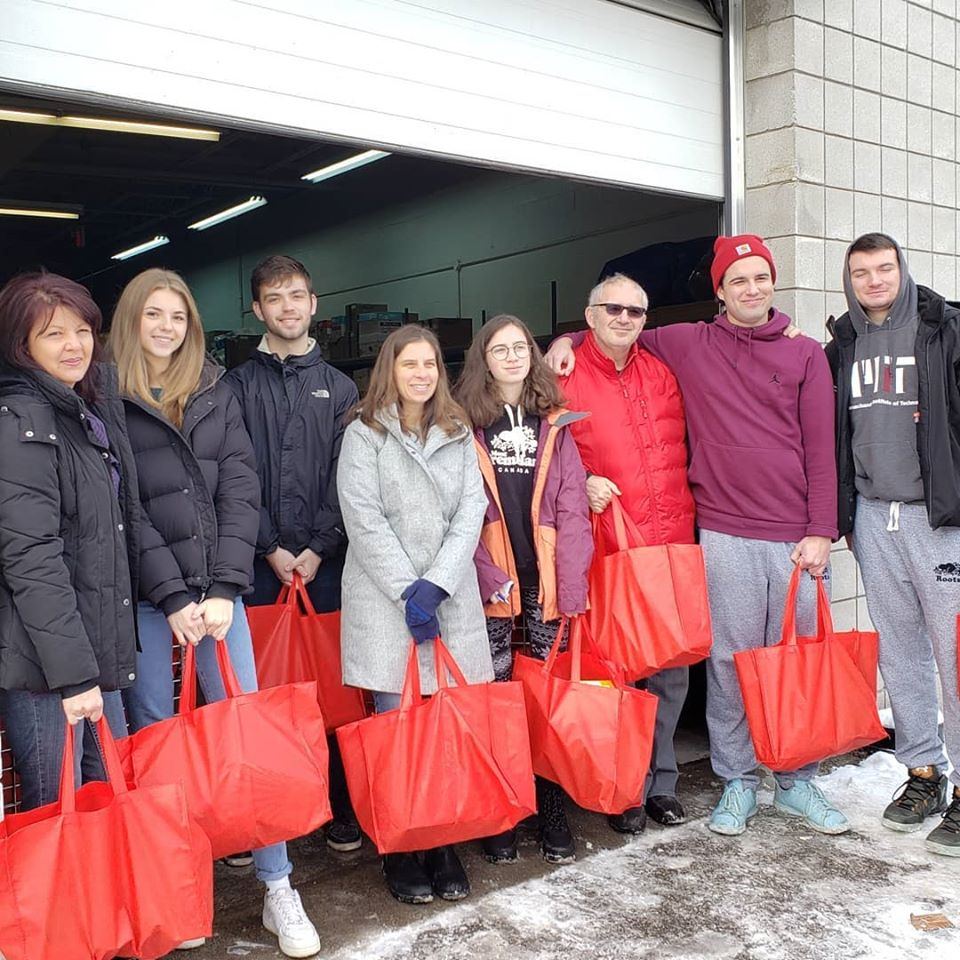 A family of volunteers with filled red bags outside a food bank loading dock